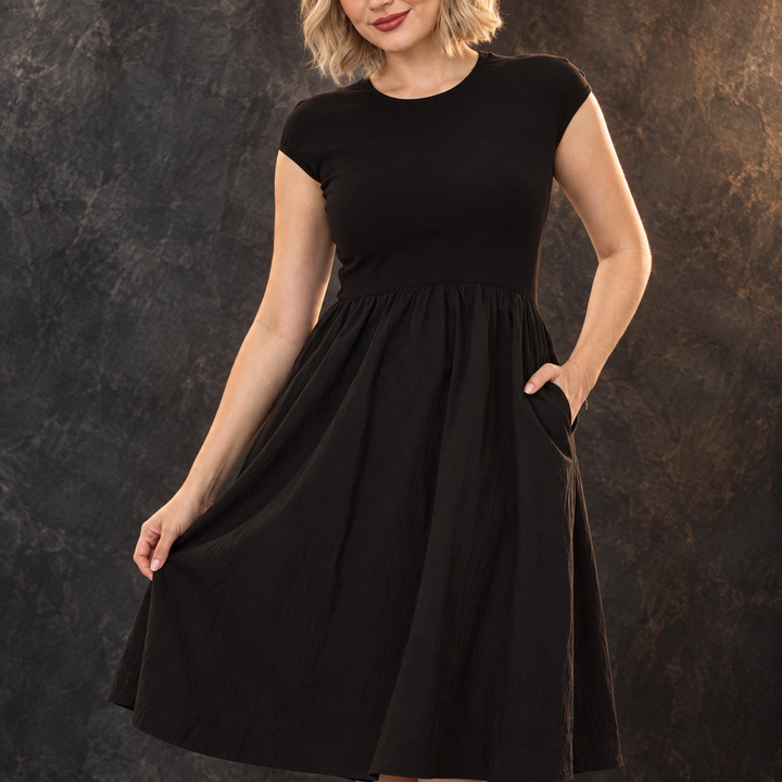 Model wearing a black cap-sleeve midi dress with full skirt — White Mark